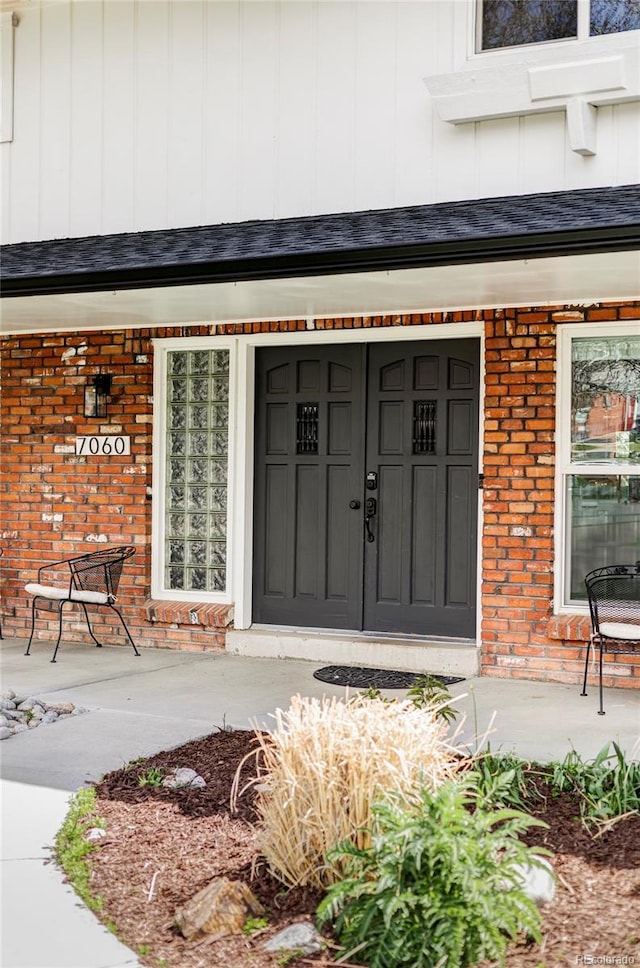 view of exterior entry featuring a porch, brick siding, and board and batten siding