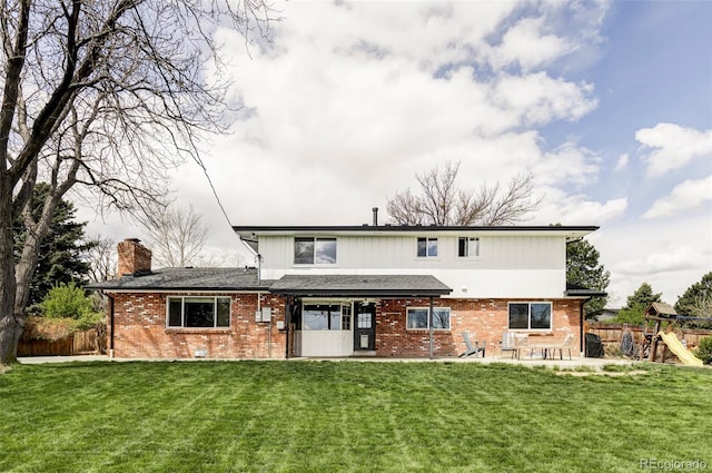 rear view of house with fence, a lawn, and brick siding