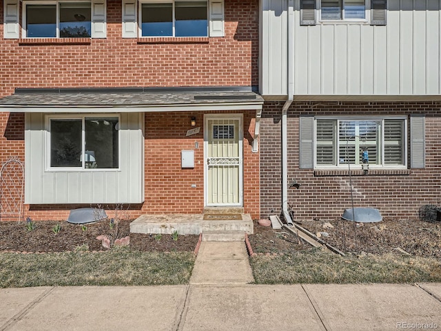 doorway to property featuring brick siding and a shingled roof