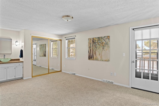 unfurnished bedroom with light colored carpet, ensuite bathroom, sink, and a textured ceiling