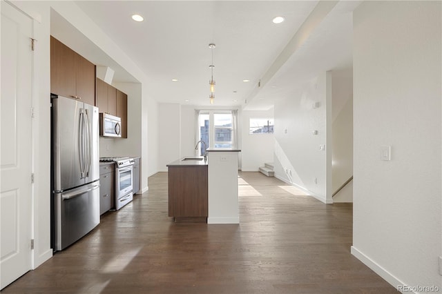 kitchen with dark hardwood / wood-style flooring, stainless steel appliances, a kitchen island with sink, sink, and hanging light fixtures