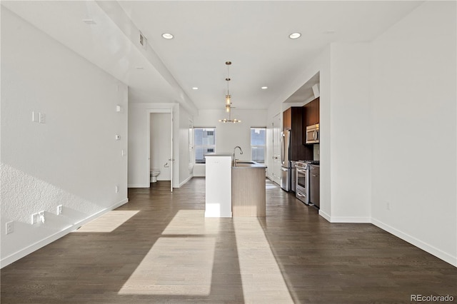 kitchen featuring stainless steel appliances, sink, dark hardwood / wood-style floors, hanging light fixtures, and an island with sink