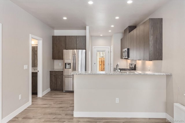 kitchen featuring kitchen peninsula, appliances with stainless steel finishes, light stone counters, radiator heating unit, and light hardwood / wood-style floors