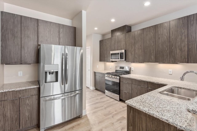 kitchen with light stone countertops, sink, stainless steel appliances, light hardwood / wood-style flooring, and dark brown cabinets