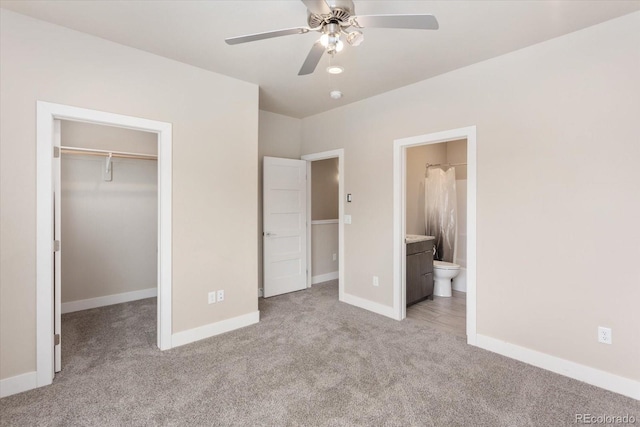 unfurnished bedroom featuring ensuite bathroom, light colored carpet, ceiling fan, a spacious closet, and a closet