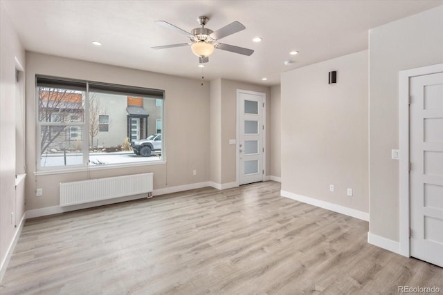 empty room featuring radiator heating unit, baseboards, wood finished floors, and recessed lighting