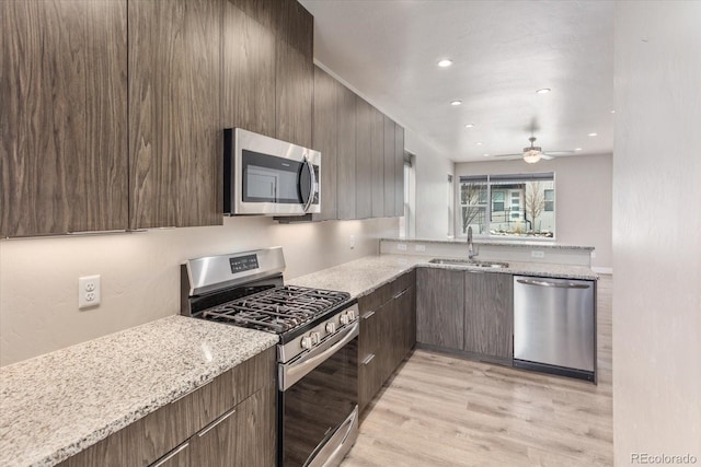 kitchen with light stone counters, stainless steel appliances, light wood-style flooring, a sink, and modern cabinets