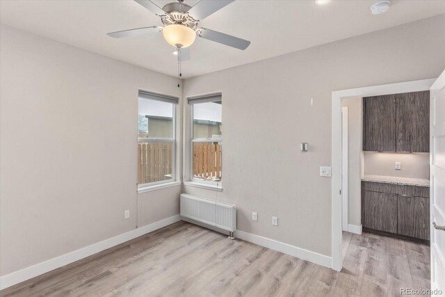 spare room featuring radiator heating unit, baseboards, light wood-style flooring, and a ceiling fan