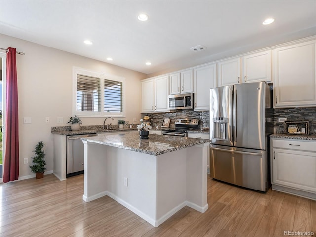 kitchen featuring tasteful backsplash, light hardwood / wood-style flooring, appliances with stainless steel finishes, a kitchen island, and white cabinets