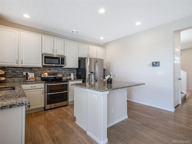 kitchen with white cabinetry, stainless steel appliances, a center island, and dark stone counters