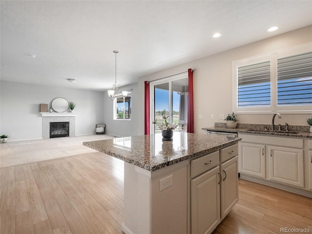 kitchen with sink, light hardwood / wood-style flooring, stone counters, hanging light fixtures, and a center island