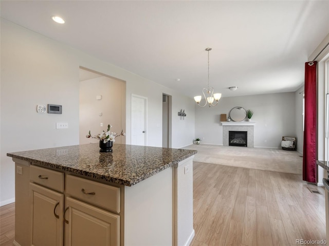 kitchen with pendant lighting, dark stone countertops, light hardwood / wood-style floors, a kitchen island, and a chandelier