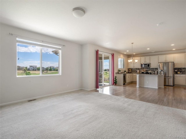 unfurnished living room featuring plenty of natural light, a chandelier, and light carpet