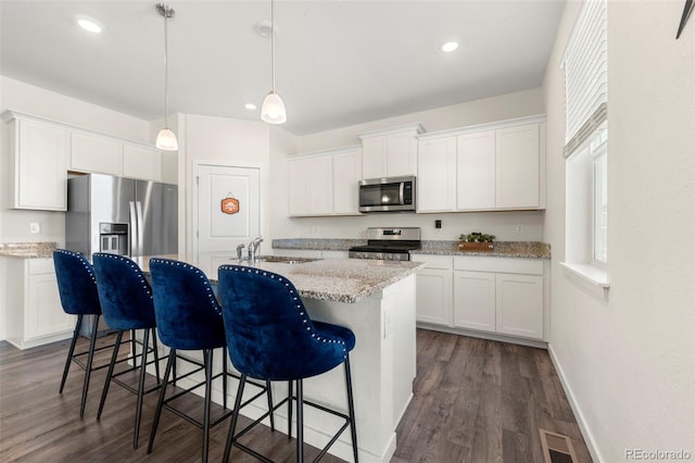 kitchen featuring white cabinets, pendant lighting, stainless steel appliances, and an island with sink