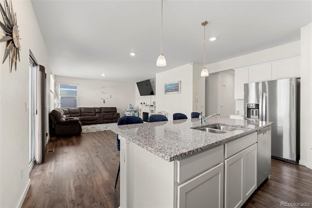 kitchen with light stone counters, sink, white cabinets, and a center island with sink