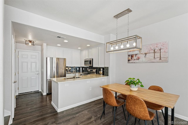 kitchen with white cabinets, decorative light fixtures, dark hardwood / wood-style flooring, stainless steel appliances, and kitchen peninsula