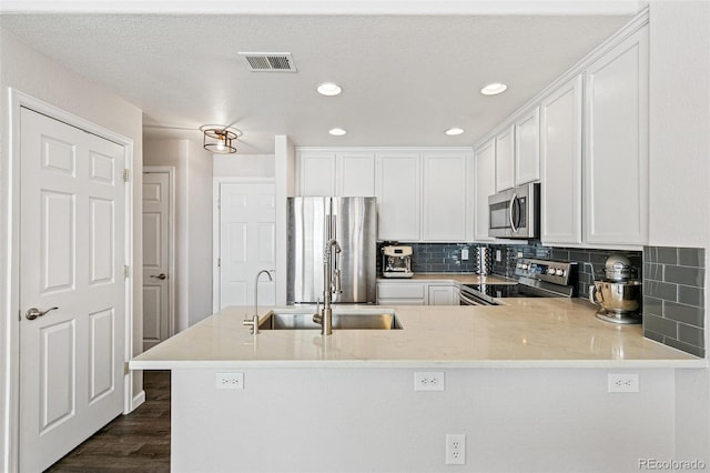 kitchen featuring white cabinetry, kitchen peninsula, stainless steel appliances, backsplash, and sink