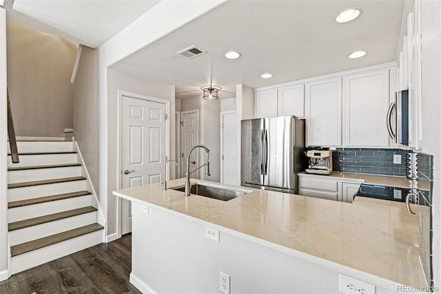 kitchen with kitchen peninsula, sink, white cabinetry, appliances with stainless steel finishes, and light stone counters