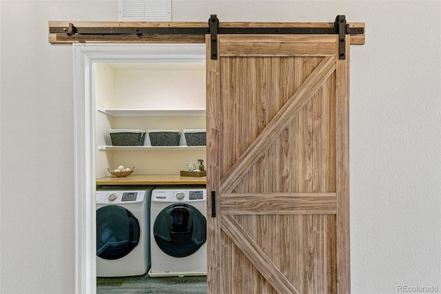 clothes washing area with washer and clothes dryer, hardwood / wood-style flooring, and a barn door