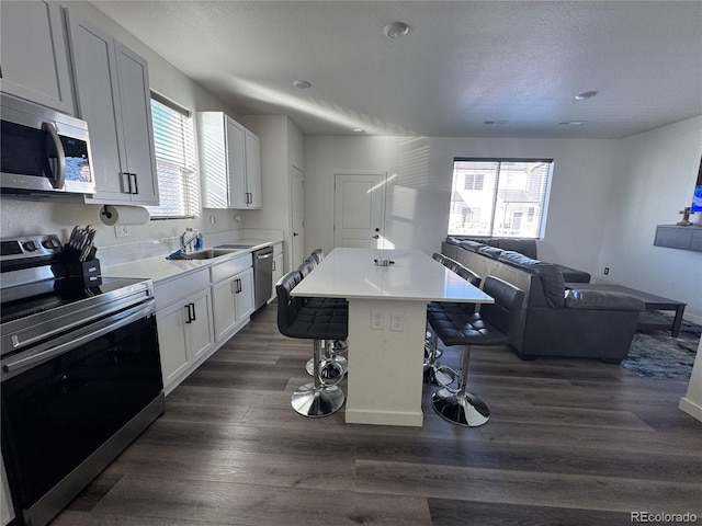 kitchen with appliances with stainless steel finishes, dark hardwood / wood-style floors, a breakfast bar, white cabinets, and a center island