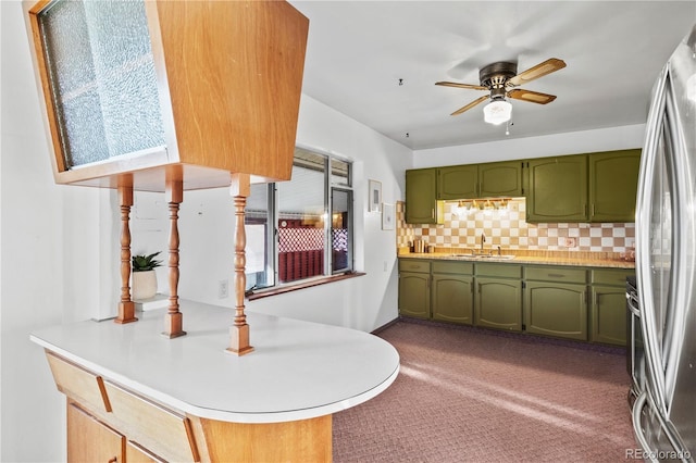 kitchen featuring green cabinetry, a peninsula, a sink, light countertops, and tasteful backsplash