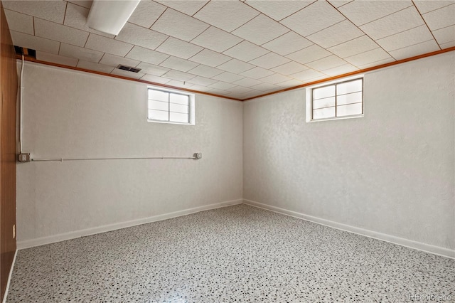 basement featuring visible vents, baseboards, and a textured wall