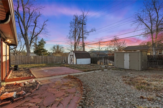 yard at dusk featuring an outbuilding, a patio, a storage shed, and a fenced backyard