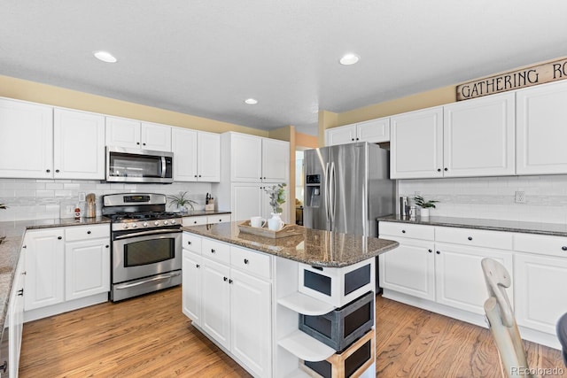 kitchen featuring appliances with stainless steel finishes, white cabinetry, a kitchen island, dark stone counters, and light wood-type flooring