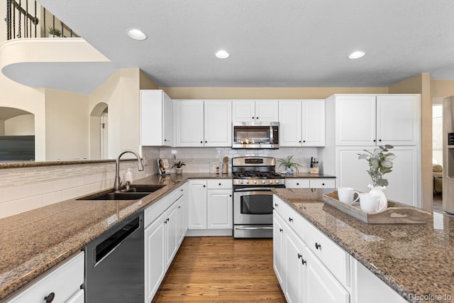 kitchen with sink, appliances with stainless steel finishes, backsplash, hardwood / wood-style floors, and white cabinets