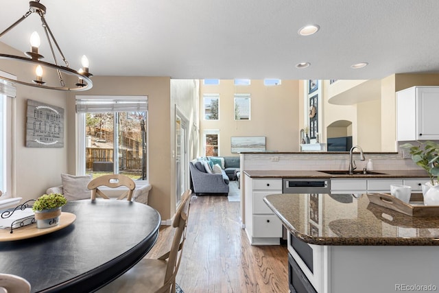 kitchen with pendant lighting, tasteful backsplash, white cabinetry, sink, and light hardwood / wood-style floors