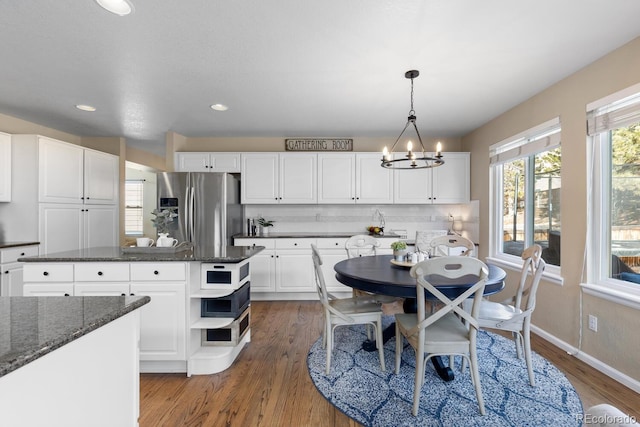 kitchen with decorative light fixtures, stainless steel fridge with ice dispenser, dark stone countertops, a kitchen island, and white cabinets