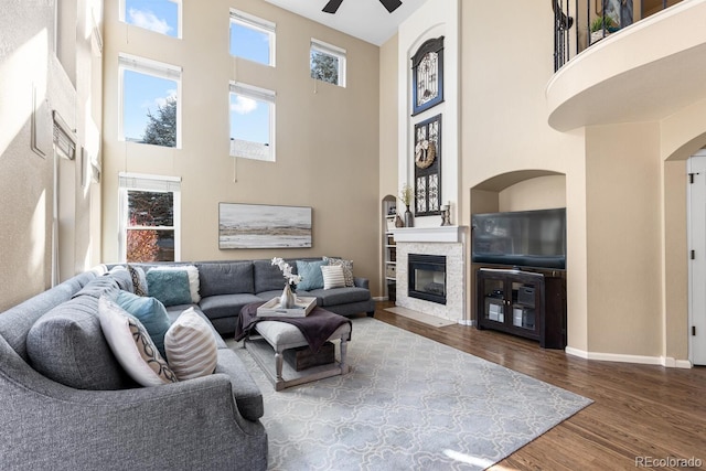 living room featuring hardwood / wood-style flooring, a stone fireplace, a high ceiling, and ceiling fan