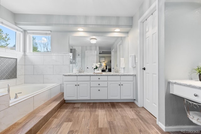 bathroom featuring vanity, wood-type flooring, and tiled tub