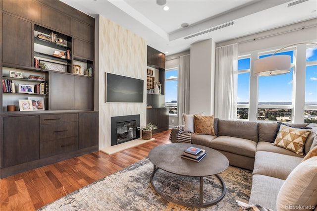 living area with recessed lighting, a fireplace, visible vents, built in shelves, and wood finished floors