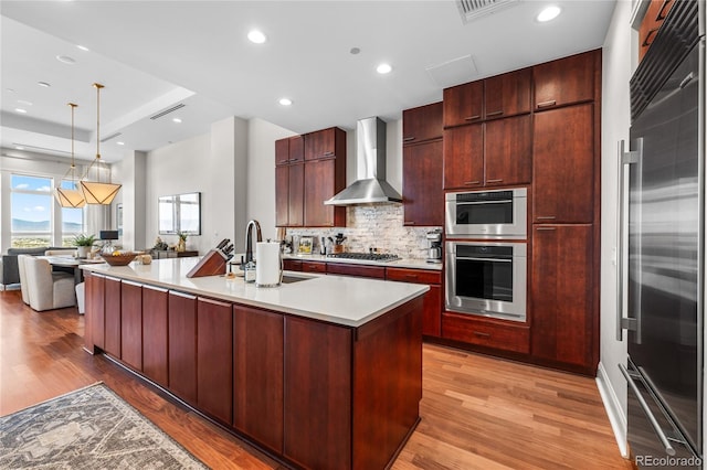 kitchen featuring light wood-type flooring, wall chimney exhaust hood, a sink, and appliances with stainless steel finishes