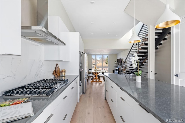 kitchen featuring stainless steel gas stovetop, decorative backsplash, light wood-style floors, white cabinets, and wall chimney exhaust hood