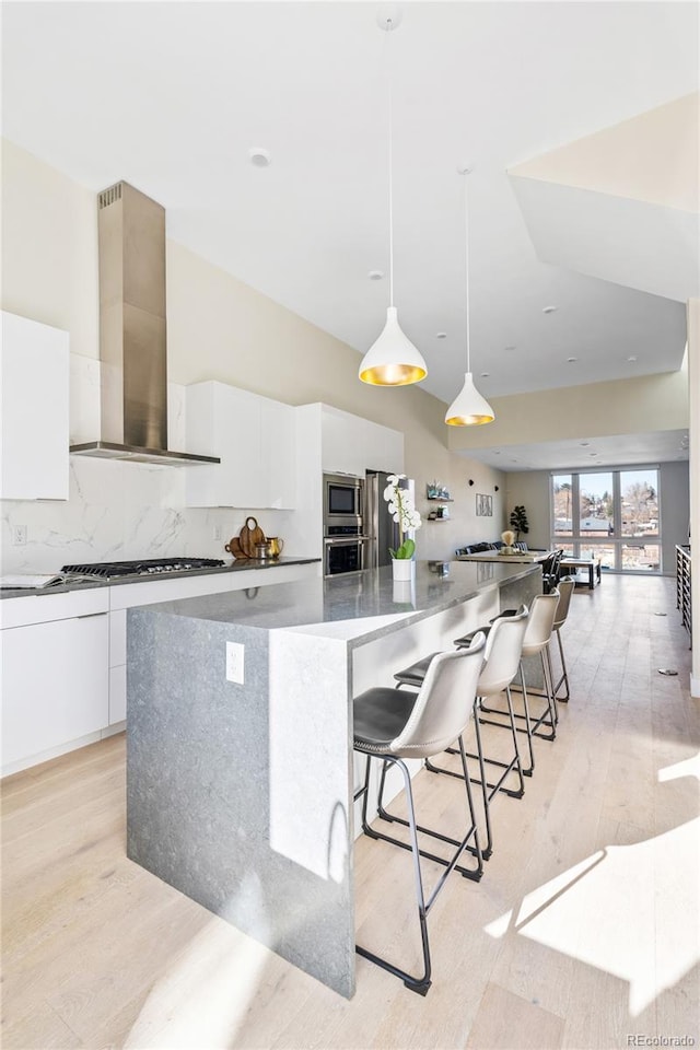 kitchen featuring a large island, light wood finished floors, tasteful backsplash, white cabinetry, and wall chimney exhaust hood