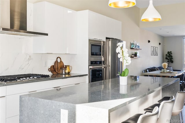 kitchen with wall chimney exhaust hood, modern cabinets, appliances with stainless steel finishes, and decorative backsplash