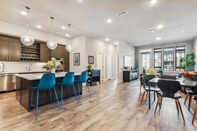 kitchen featuring dark brown cabinets, a kitchen island, appliances with stainless steel finishes, a kitchen breakfast bar, and light hardwood / wood-style flooring