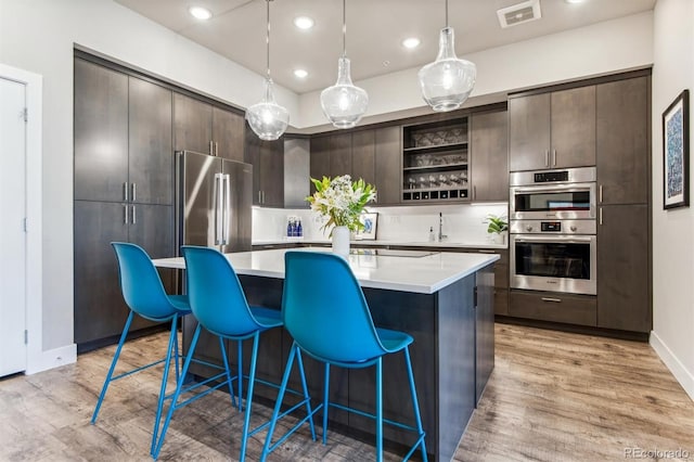 kitchen with appliances with stainless steel finishes, a kitchen island, dark brown cabinets, light hardwood / wood-style floors, and pendant lighting