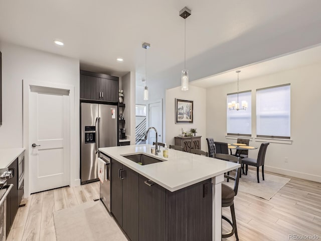 kitchen featuring dark brown cabinetry, stainless steel appliances, sink, decorative light fixtures, and light hardwood / wood-style flooring