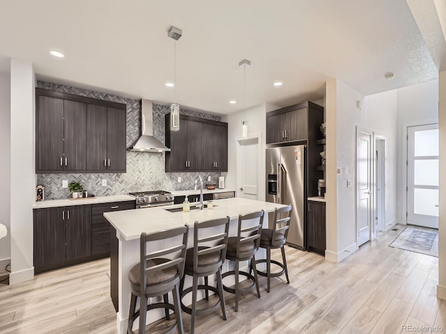 kitchen featuring high end appliances, decorative light fixtures, wall chimney exhaust hood, dark brown cabinets, and light hardwood / wood-style floors