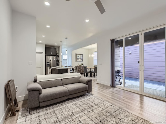 living room featuring light hardwood / wood-style flooring, a healthy amount of sunlight, and ceiling fan with notable chandelier