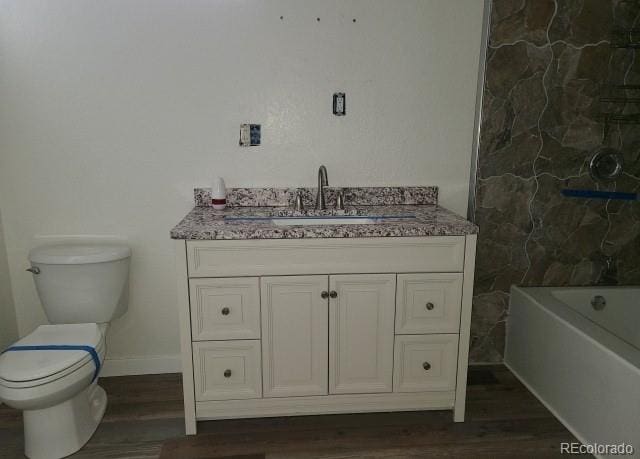 bathroom with a tub to relax in, wood finished floors, vanity, baseboards, and toilet