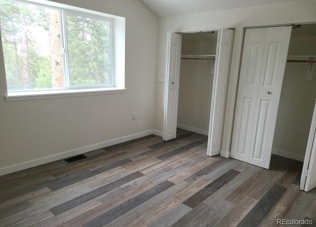 unfurnished bedroom with dark hardwood / wood-style floors, vaulted ceiling, multiple windows, and multiple closets