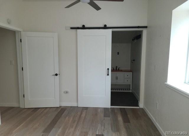 unfurnished bedroom featuring a barn door, ceiling fan, ensuite bath, and wood-type flooring