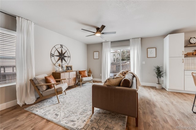 living area with light wood-style floors, ceiling fan, and baseboards