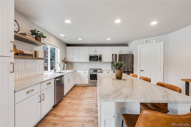 kitchen with a breakfast bar, stainless steel appliances, visible vents, a sink, and a kitchen island