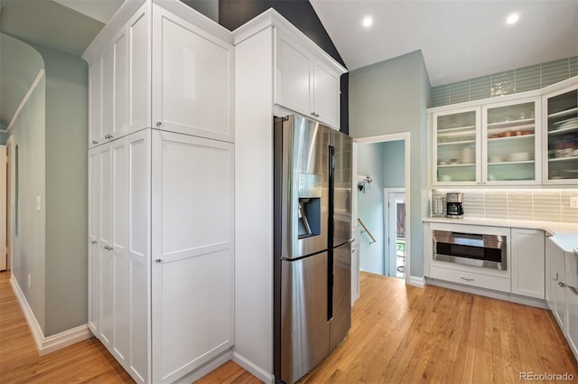 kitchen with stainless steel fridge with ice dispenser, oven, decorative backsplash, white cabinetry, and light wood finished floors