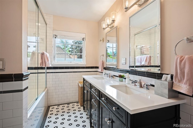 bathroom featuring a tile shower, tile walls, double vanity, and wainscoting